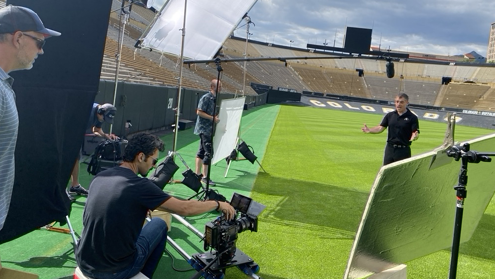 Snowy Peak Films crew filming a Wilhite Law Firm commercial on the field at Folsom Field in Boulder, with a cinema camera on a dolly, diffusion, bounce boards and a boom mic
