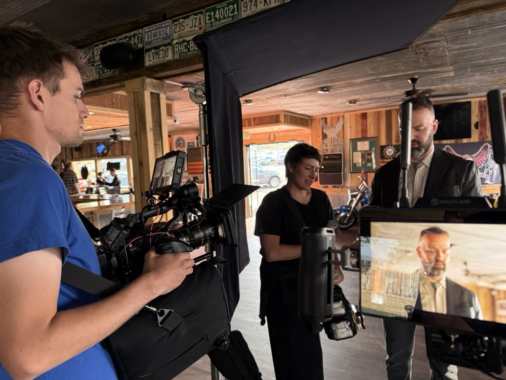 Snowy Peak Films crew filming a commercial for The Outlaw Injury Attorneys at the Stagecoach Saloon in Franktown, Colorado, with a cinema camera, flags and an on-set monitor