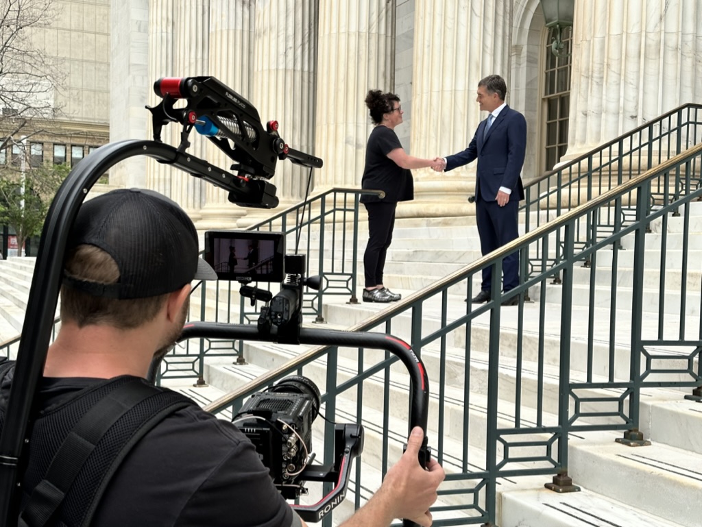 Camera operator with a gimbal-stabilized cinema camera filming a handshake for The Wilhite Law Firm on the steps of the Byron White United States Courthouse in Denver