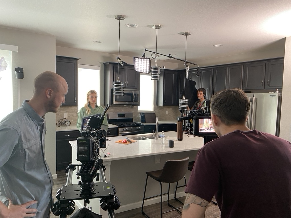 Snowy Peak Films crew filming a commercial for T47 Cutting Board in a kitchen, with two cinema cameras, overhead LED lighting and the director watching the monitor