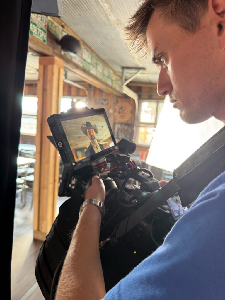 Director of Photography filming a low-angle shot of talent in a cowboy hat with a Sony FX6 supported by a SAKK camera saddle